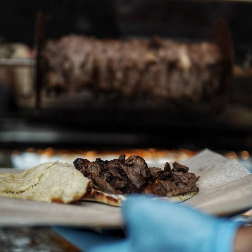 Baba's Kebab meat and pita bread being prepared, with a kebab rotisserie in the background.