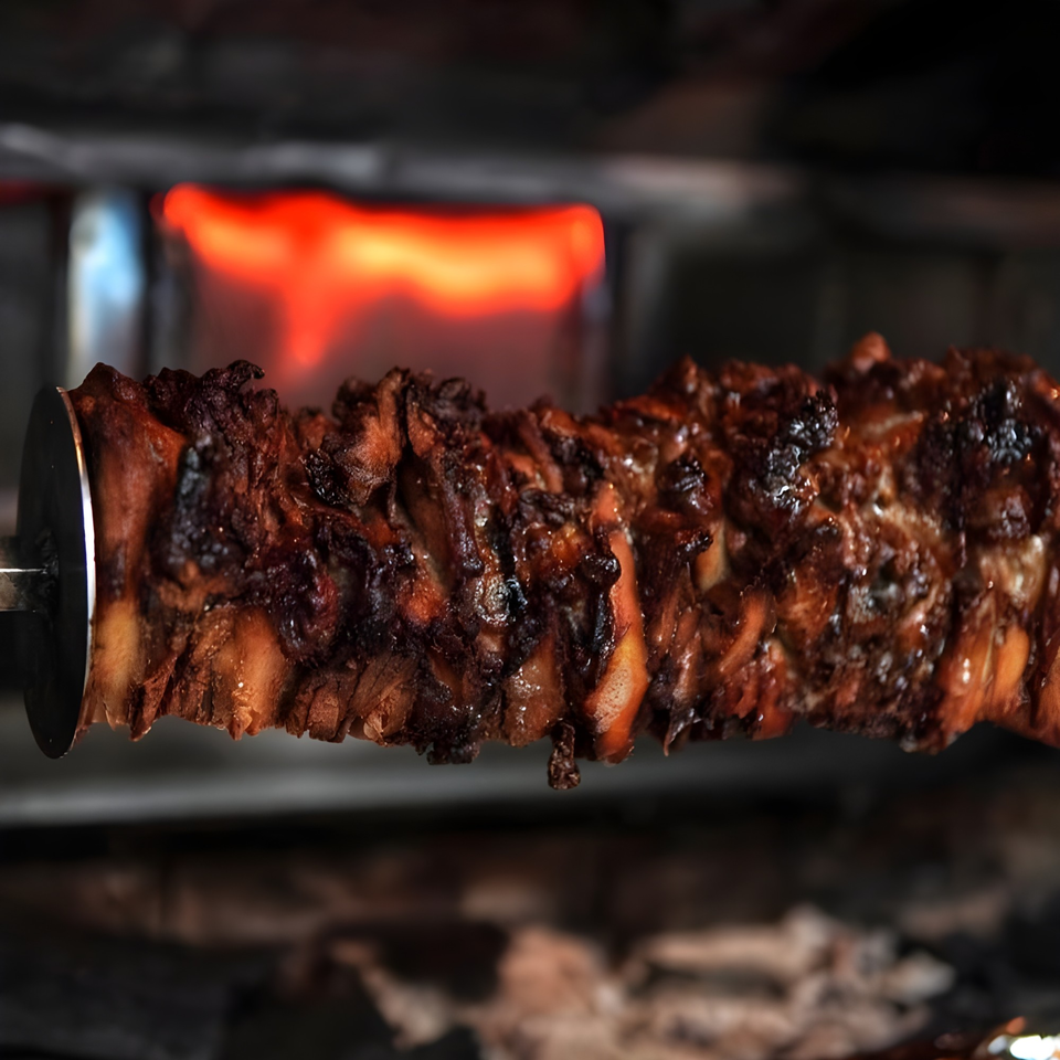Baba's Kebab meat rotating on a vertical spit, cooking with a fiery red glow in the background.